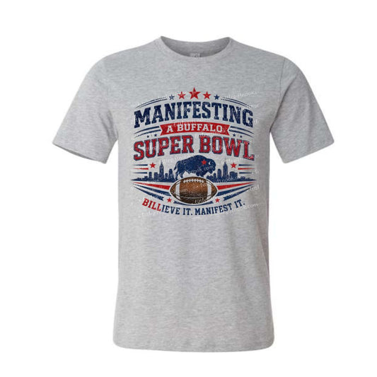 Gray tshirt with red and blue "Manifesting a Buffalo Super Bowl Billieve it manifest it" design on front on a white background.