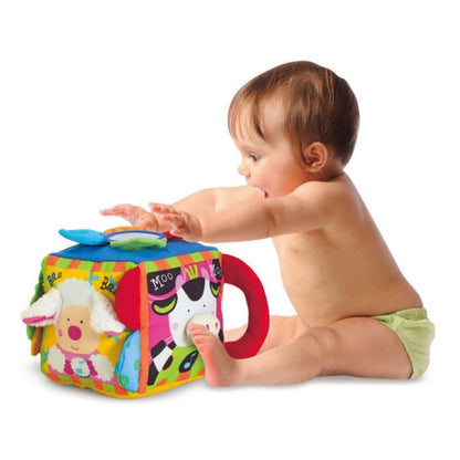 Baby playing with Melissa & Doug soft Musical Farm Cube toy sitting on white background.
