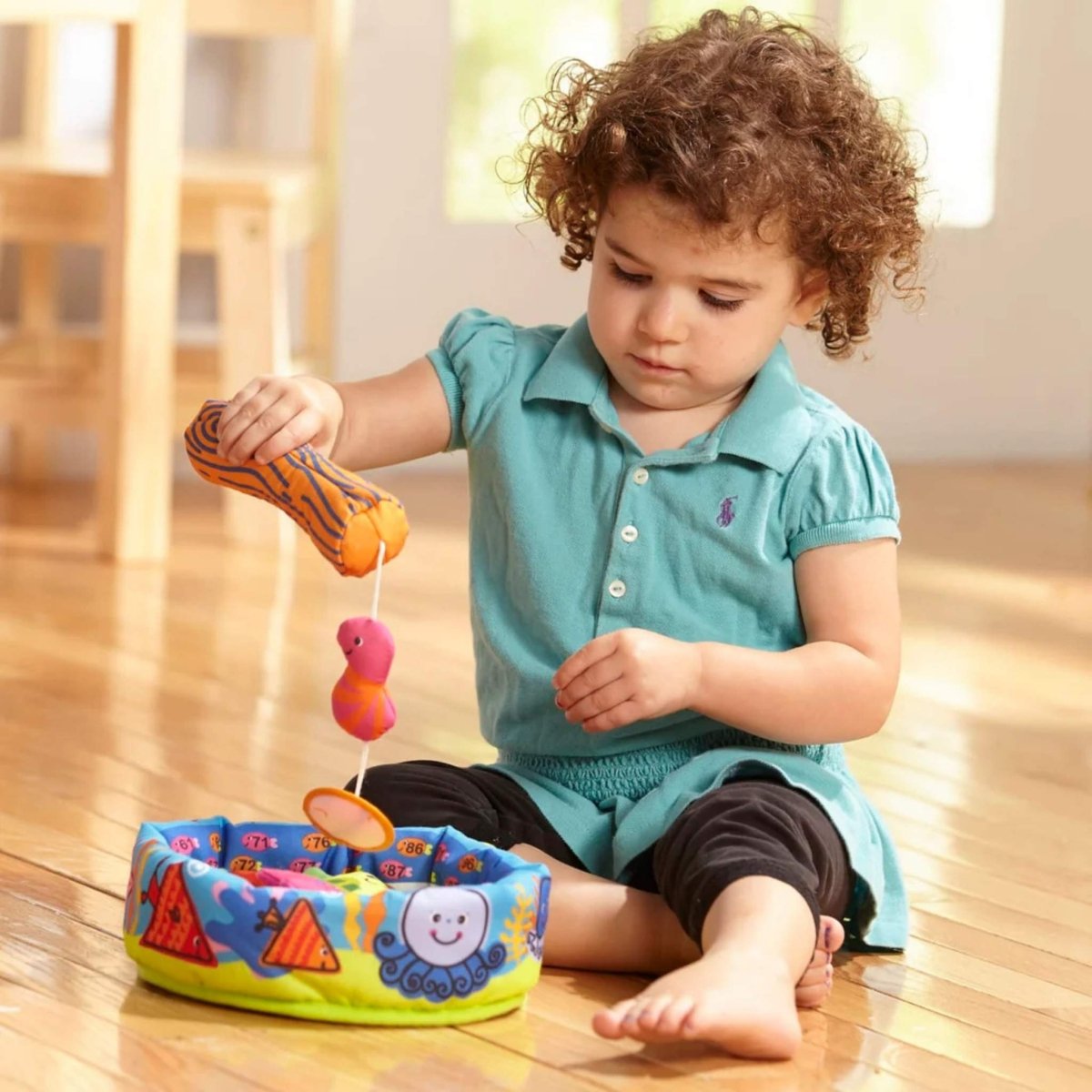 Child playing with Melissa & Doug Fish & Count soft fishing set game on a wood floor.