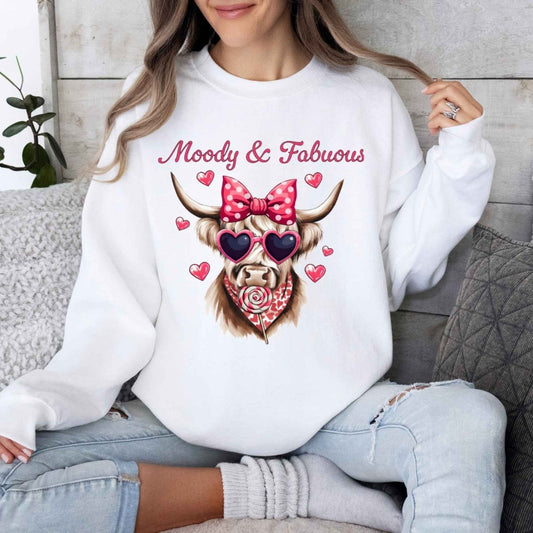 Woman wearing white sweatshirt with pink highland cow in bow and sucker moody and fabulous on front. Little Gift Nook