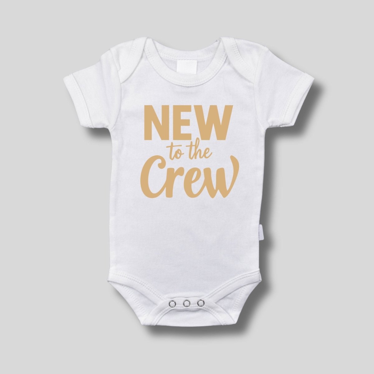 White baby bodysuit with tan "New to the Crew" on front sitting on a light gray background. Little Gift Nook
