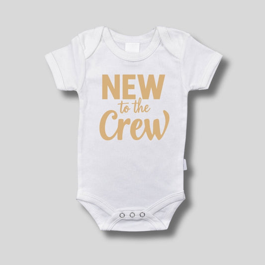 White baby bodysuit with tan "New to the Crew" on front sitting on a light gray background. Little Gift Nook