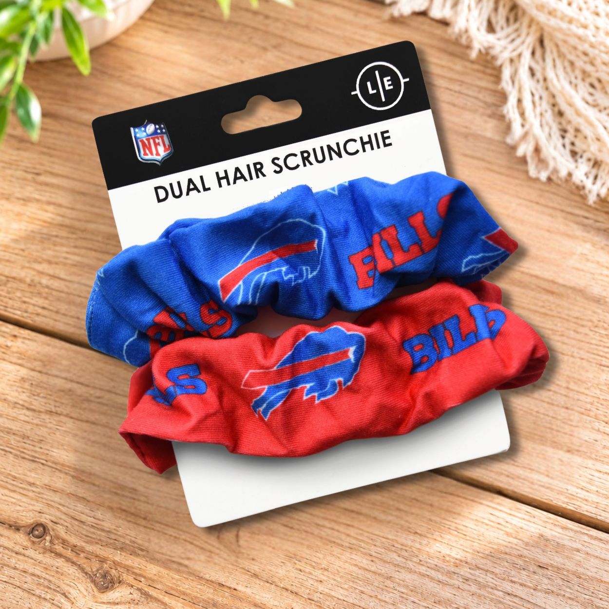 2Buffalo Bills logo scrunchies one blue one red on a product card laying on wooden surface. 