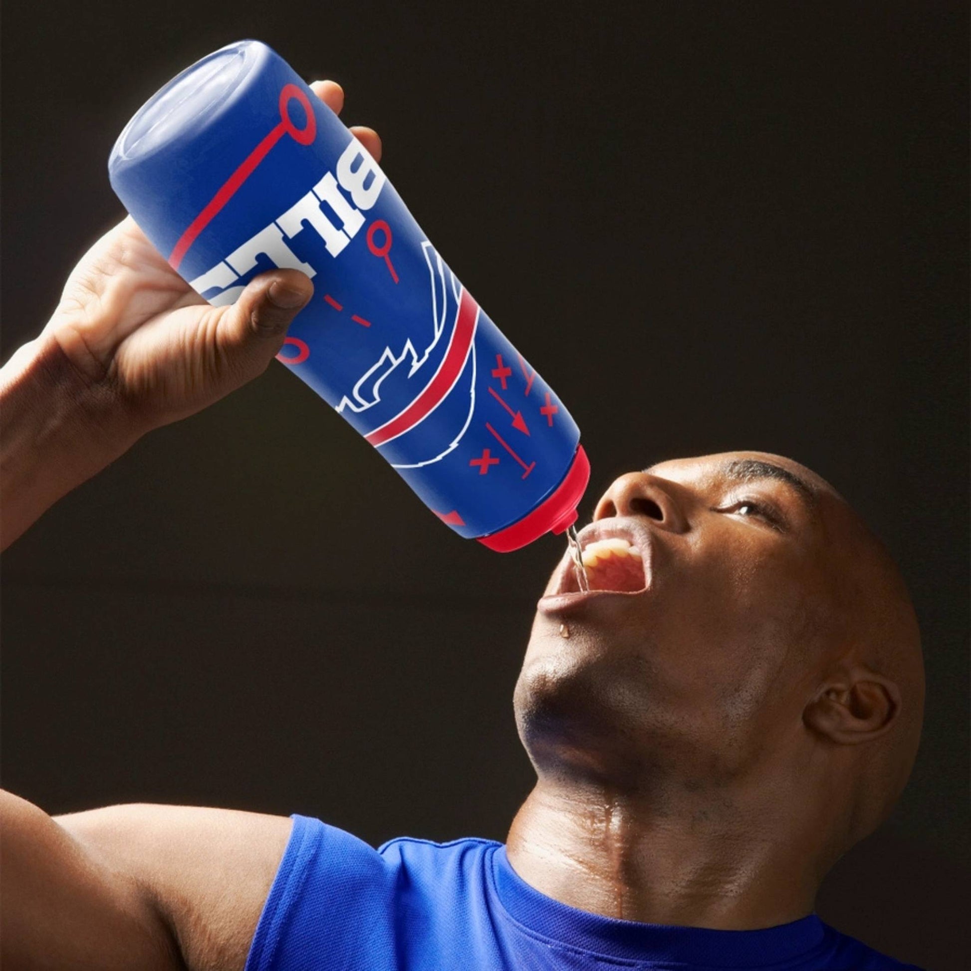 Person holding Buffalo Bills squeezy logo plastic water bottle squirting water into his mouth on a gray background.