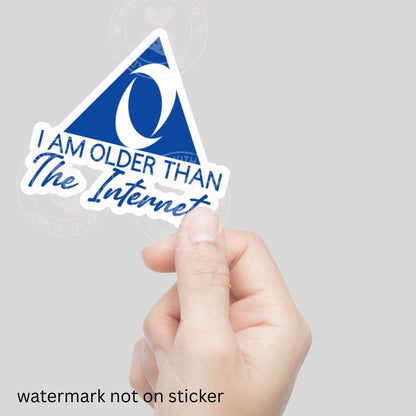 Hand holding a sticker with text 'I AM OLDER THAN The Internet' blue and white sticker against a gray background