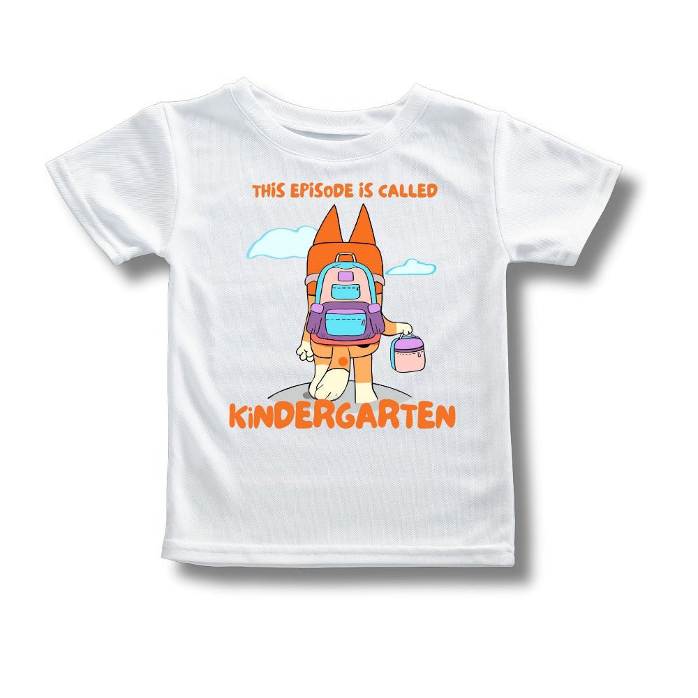White kids t-shirt with orange dog carrying a backpack and lunchbox with orange text "This episode is called Kindergarten" on front laying on a white background. 