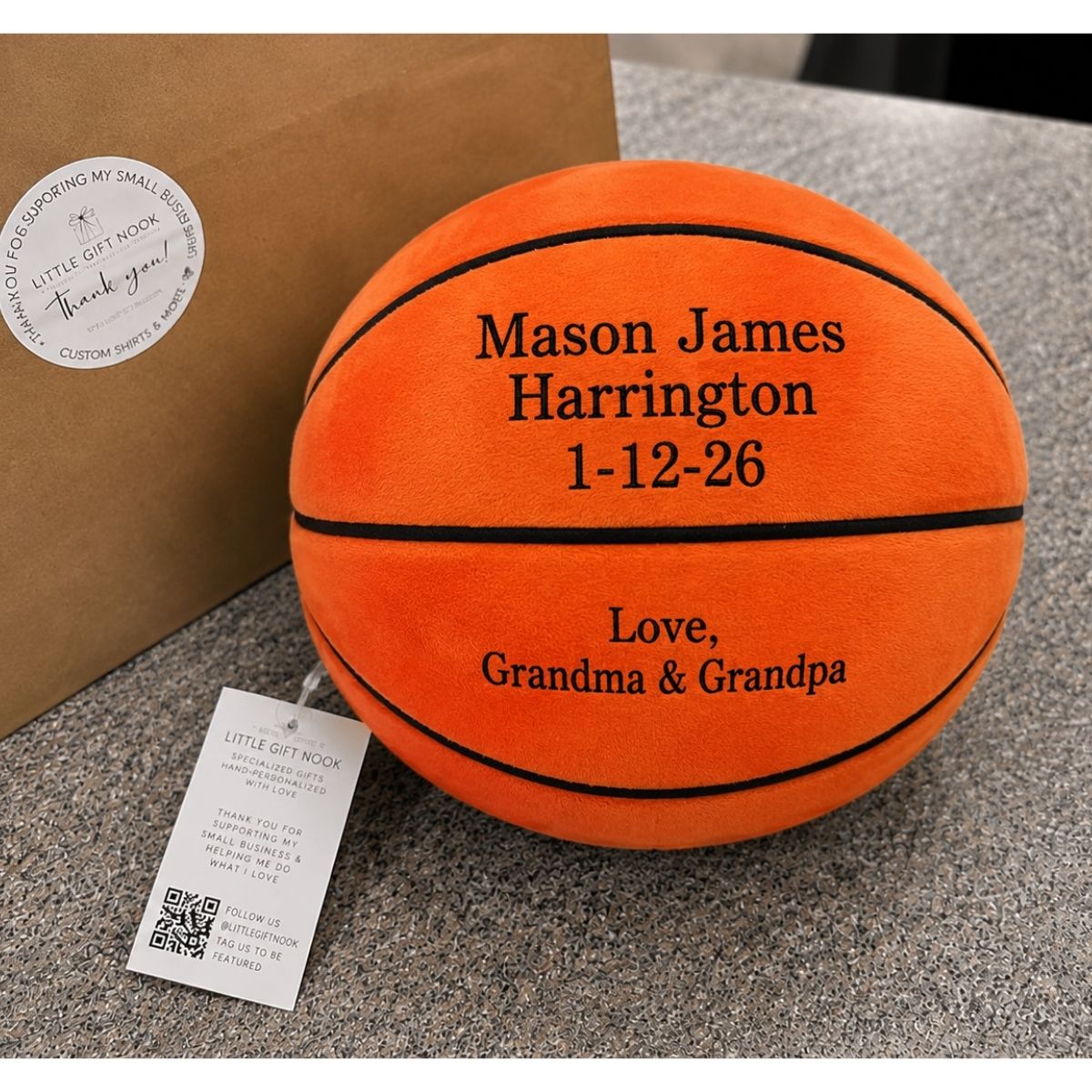 Personalized plush orange basketball with child's name, date of birth, and love Grandma & Grandpa message on counter and next to shopping bag. 