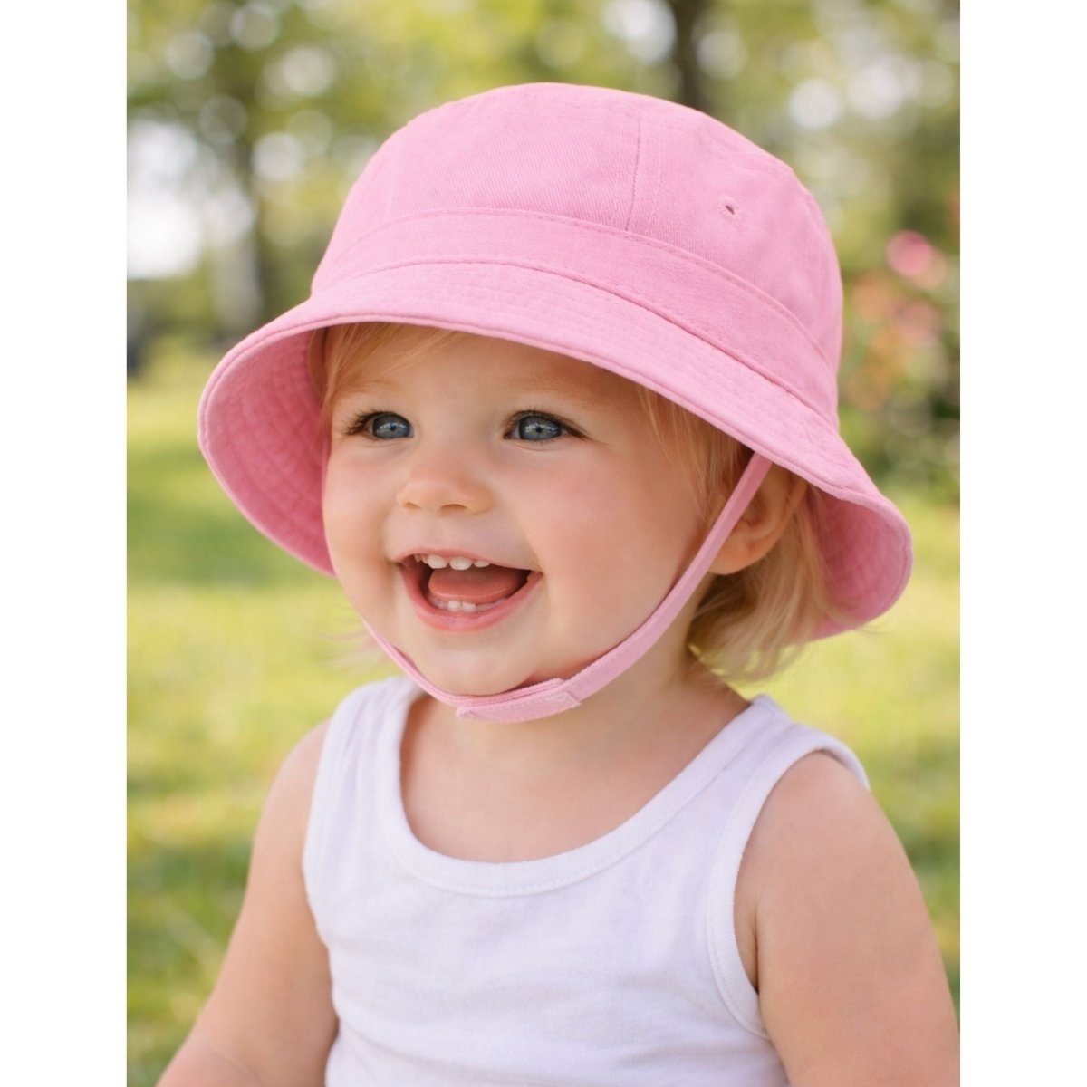 Baby wearing pink bucket sun hat with chin strap outdoors.