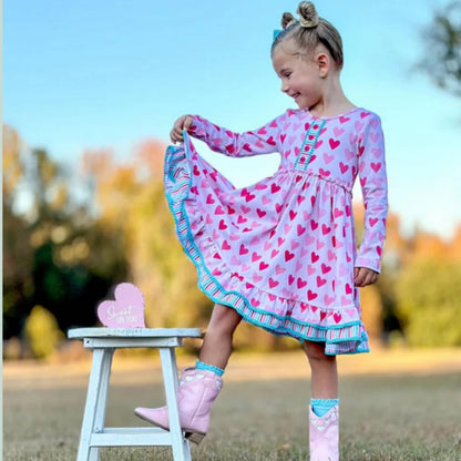 Pink Blue Hearts Ruffle Twirl Dress. Girl modeling dress and pulling at the ruffles. Cotton/Spandex blend 2 pink heart print dress with blue striped accents & ruffle hem.  Pull on/ off.  Buttery soft & Stretchy.  Little Gift Nook.
