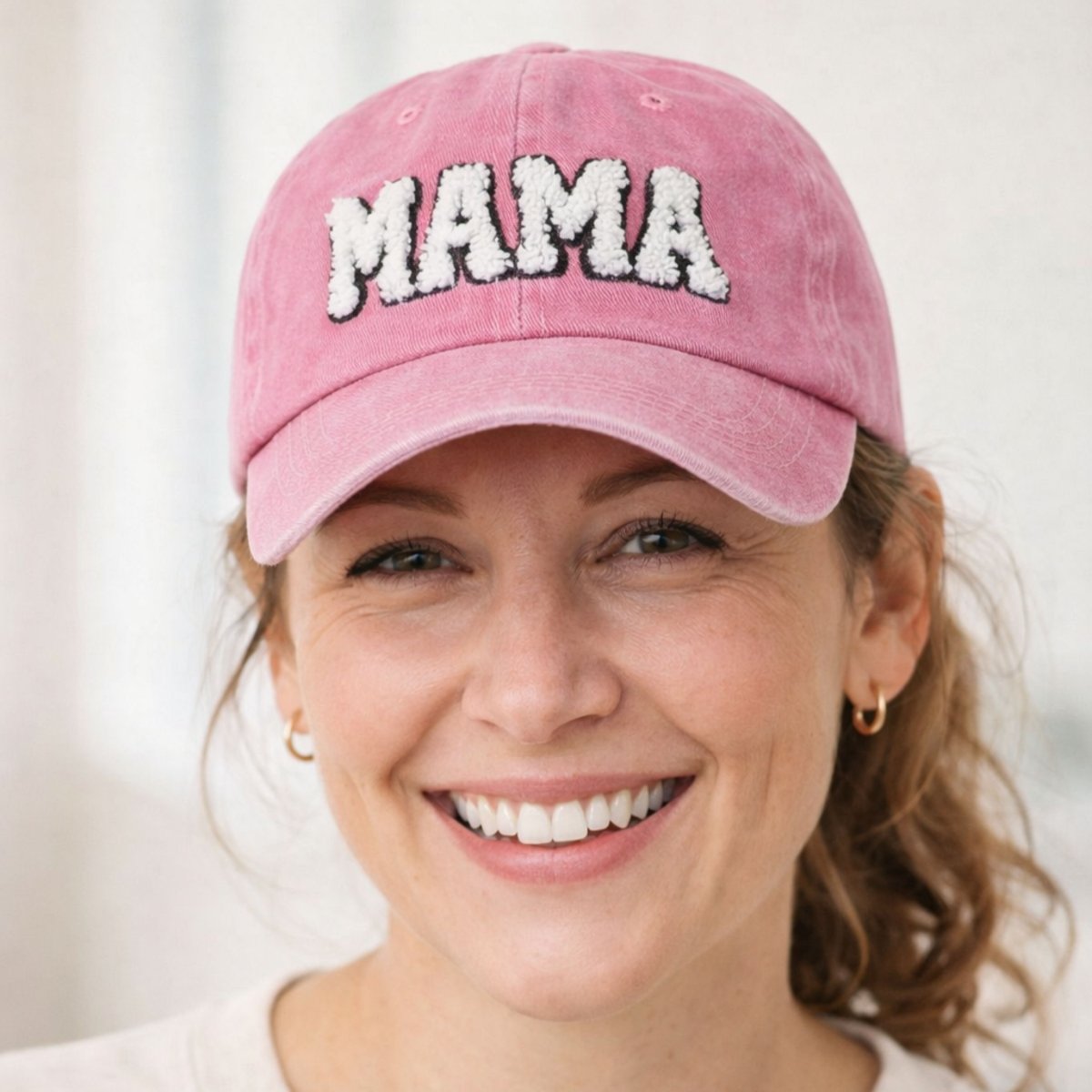 woman wearing pink sherpa letters MAMA baseball hat on a white background.