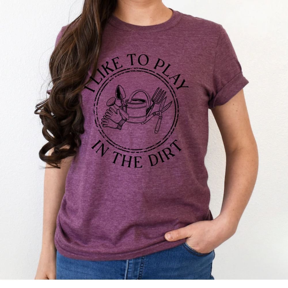 Woman wearing plum purple "I Like to Play in the Dirt"gardening tools tshirt standing on white background.