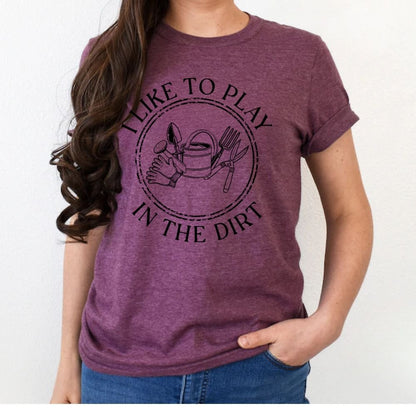 Woman wearing plum purple "I Like to Play in the Dirt"gardening tools tshirt standing on white background.