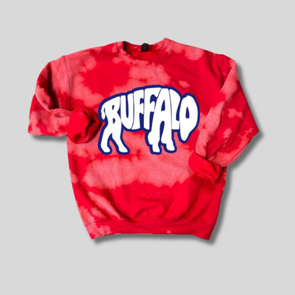 Red bleached tie dye crewneck sweatshirt with blue and white buffalo letters in shape of buffalo on front laying flat on light gray background.