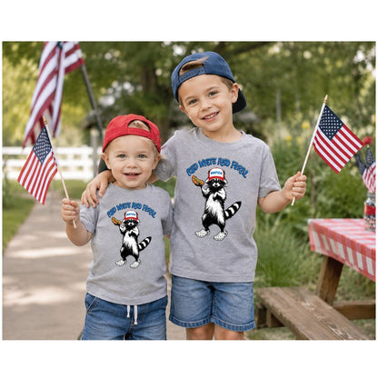 Two children wearing matching shirts with a raccoon holding a hot dog and text "Red, White, and Feral" on fronts and American flags in the background.