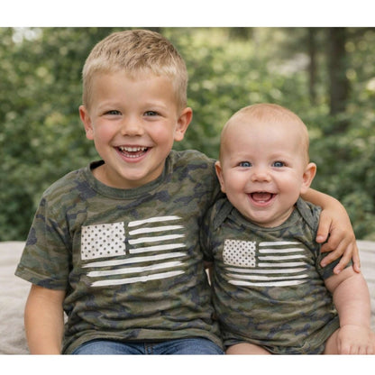 Brother's wearing matching camo american flag shirts sitting outdoors.