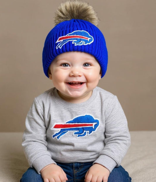 baby sitting wearing royal blue buffalo football winter pom hat on tan background. Little Gift Nook