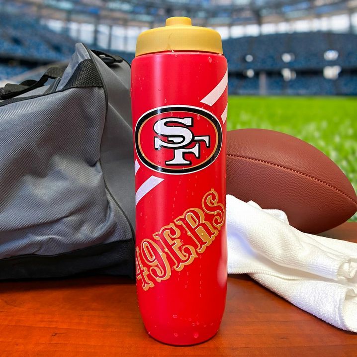 San Francisco 49ers Squeezy Water Bottle 32 ounces standing on football field sidelines.