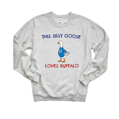 A light heather gray crewneck sweatshirt featuring a graphic of a cartoon goose wearing a blue jersey with the number 17, with the text 'THIS SILLY GOOSE' above and 'LOVES BUFFALO' below in blue and red lettering.