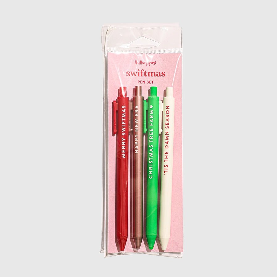 Set of four pens in red, pink, green, and white with swifite swiftmas theme text in a clear packaging on a light gray background.