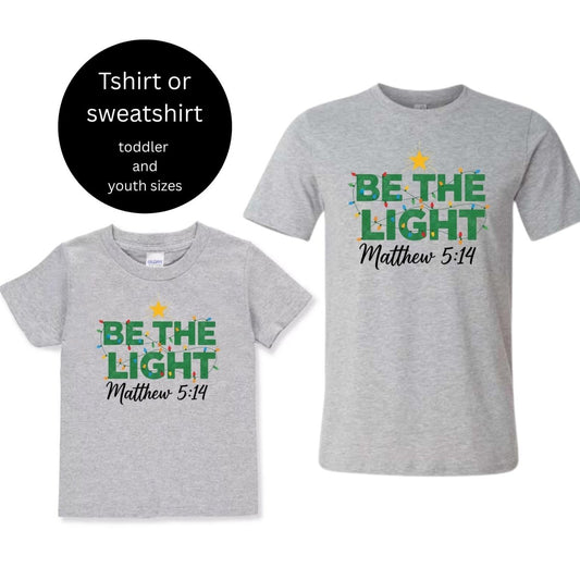 Gray toddler and youth kids Be the Light Christmas lights Matthew 5:14 tshirts sitting on white background. Little Gift Nook