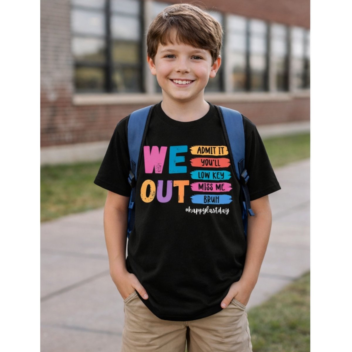 Child wearing black tshirt with color text and design "We out bruh happy last day" on front standing outdoors by school.