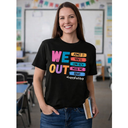 Woman teacher wearing black tshirt with colorful text and design "We out bruh happy last day" on front standing in a classroom.