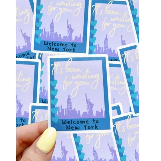 purple and blue rectangle polaroid style welcome to New York sticker being held in front of more of the same sticker background. Little Gift Nook