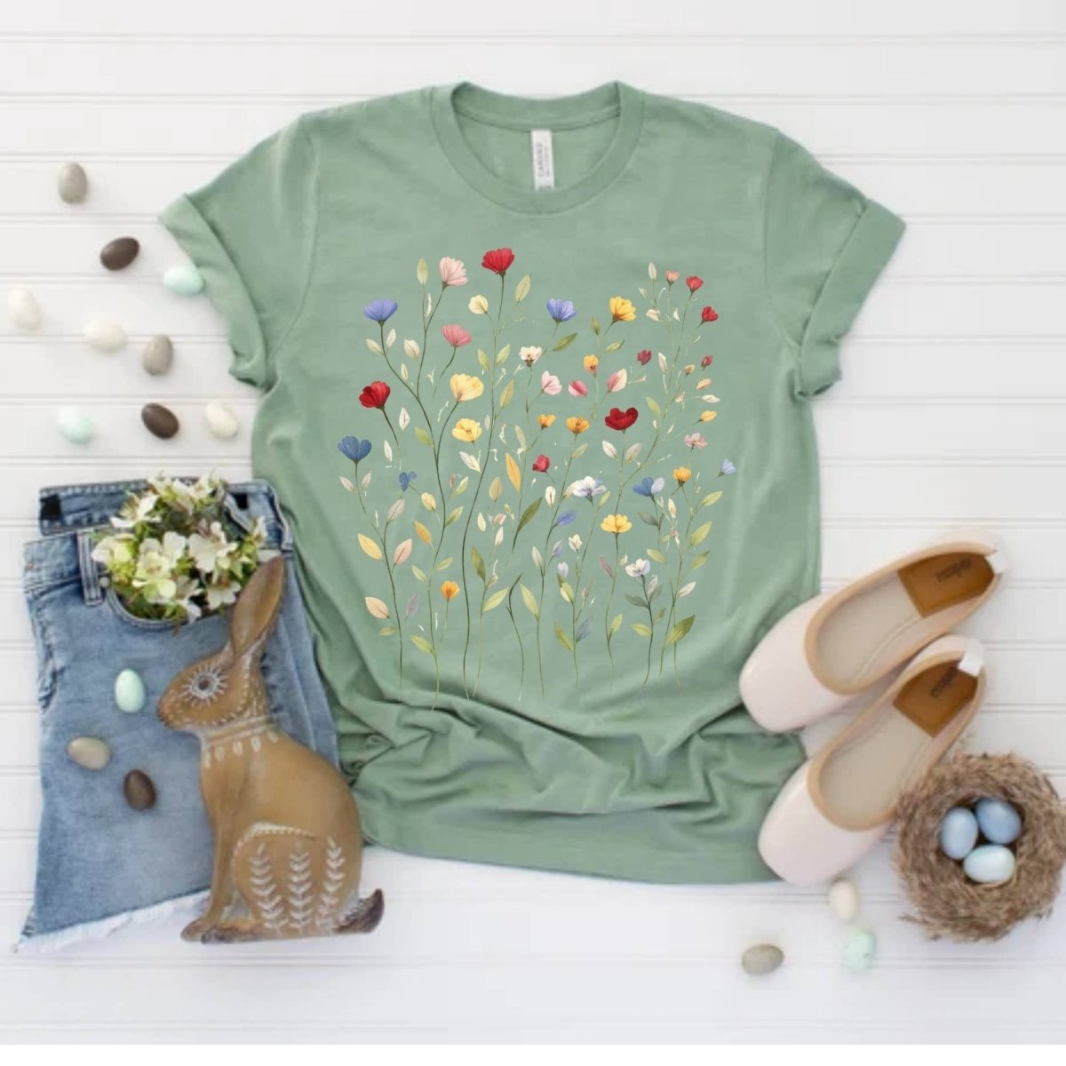 Sage green colorful wildflowers tshirt sitting on white background with easter theme eggs and bunny. 