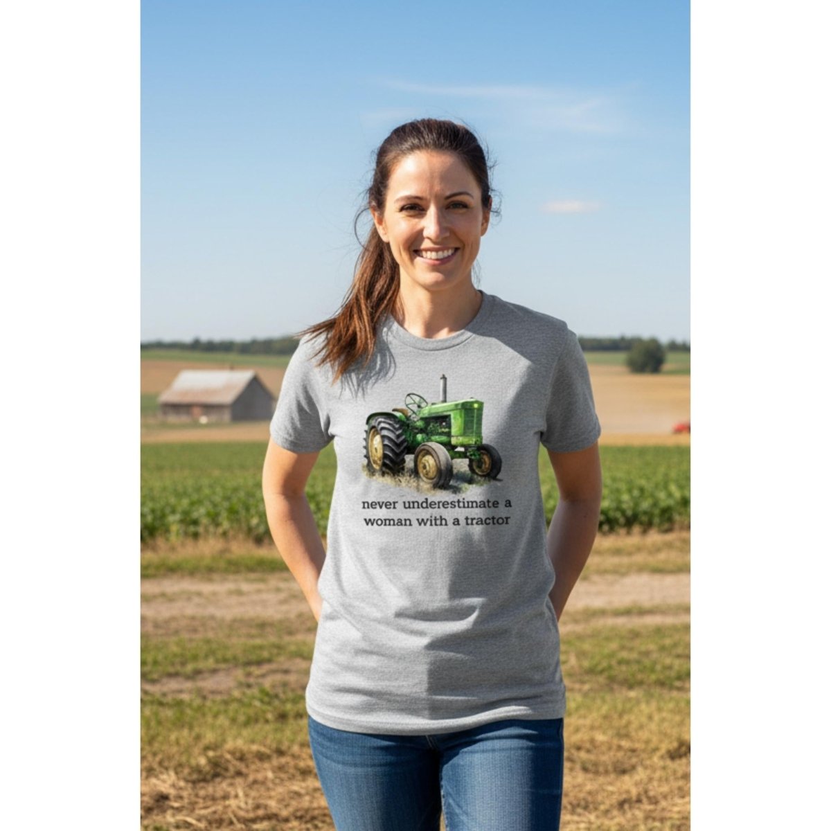 woman wearing gray tractor t-shirt with caption "never underestimate a woman with a tractor" on farm field background.