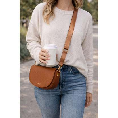 Woman wearing a beige sweater, blue jeans, and carrying a chestnut brown Kedzie lune crossbody bag purse outdoors.