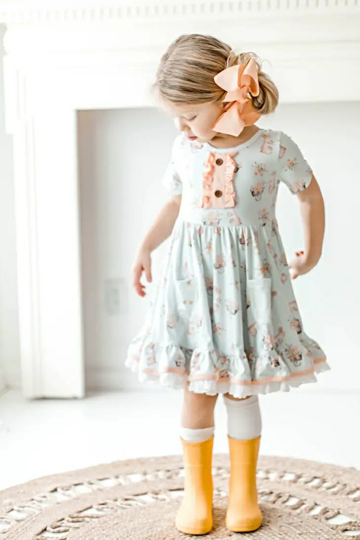 Honey Bunny Blue Eyelet Twirl Dress. Front view of dress with pink ruffle chest, bunnies printed all over dress, eyelet trim and little girl wearing dress in yellow rain boots. - Little Gift Nook