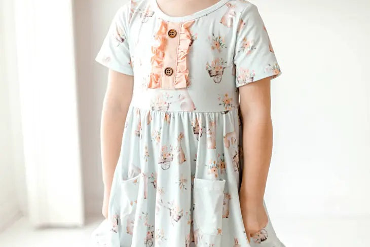Honey Bunny Blue Eyelet Twirl Dress. Close up of front of dress. Light baby blue color dress with pink ruffle chest and bunny floral print. 2 front pockets. - Little Gift Nook