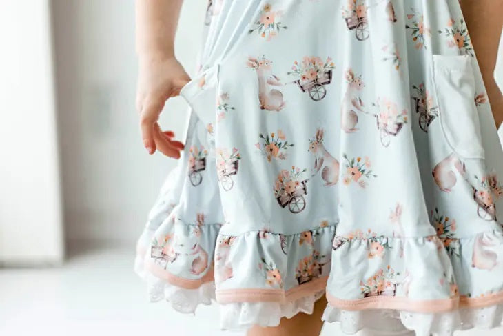 Honey Bunny Blue Eyelet Twirl Dress. Close up of pattern on dress. Light baby blue dress with pink bunnies and floral wheelbarrows. pockets. - Little Gift Nook