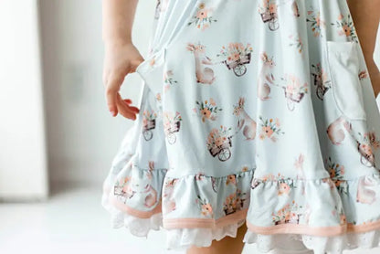 Honey Bunny Blue Eyelet Twirl Dress. Close up of pattern on dress. Light baby blue dress with pink bunnies and floral wheelbarrows. pockets. - Little Gift Nook