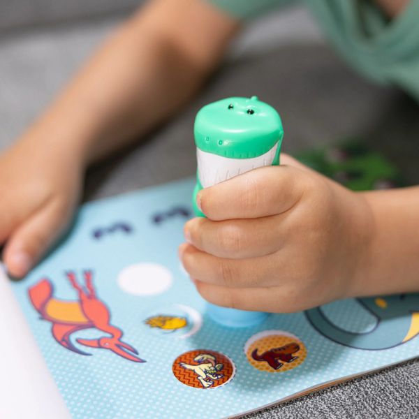 Melissa & Doug Sticker WOW Dinosaur Activity Pad. Boy using the dino theme sticker stamper that is refillable to push stickers into activity pad. - Little Gift Nook