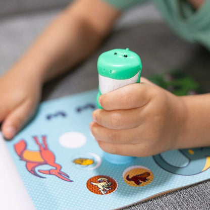 Melissa & Doug Sticker WOW Dinosaur Activity Pad. Boy using the dino theme sticker stamper that is refillable to push stickers into activity pad. - Little Gift Nook