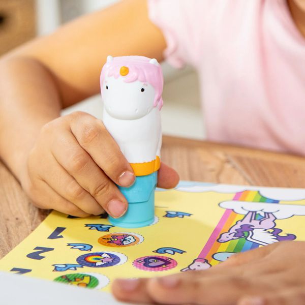 Melissa & Doug Sticker WOW Unicorn Activity Pad. Little girl holding stamper, pushing down to stamp a sticker on the pages of the activity pad. - Little Gift Nook