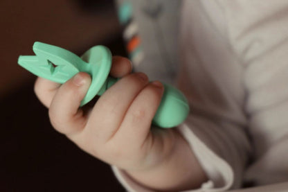 baby hand holding green baby fork utensil by the Teething Egg Company.