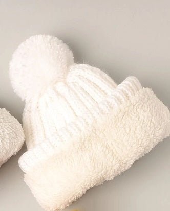 White knitted beanie with pom-pom rolled up to show sherpa interior laying on a light gray background.