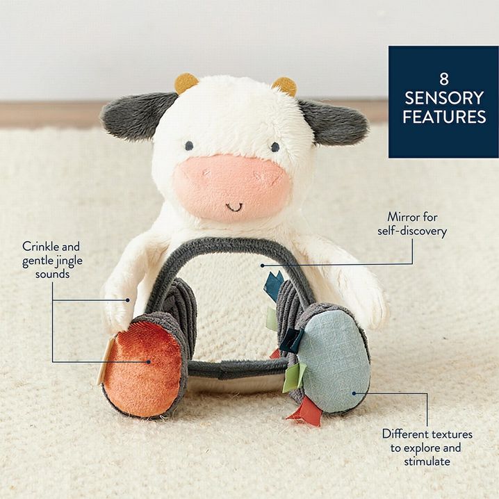 Itzy Ritzy plush  mirror cow texture baby toy.  Soft plush cow with crinkle & jingle sounds, taggies and mirror on belly sitting on creme background with features.