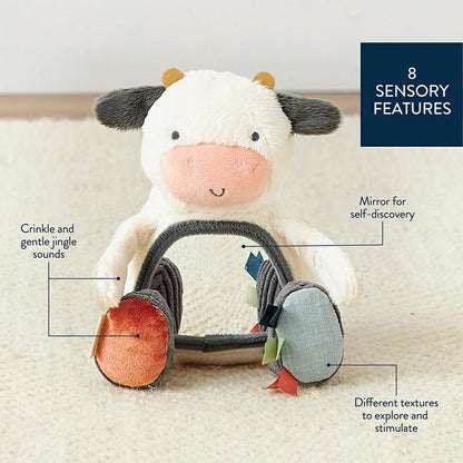 Itzy Ritzy plush  mirror cow texture baby toy.  Soft plush cow with crinkle & jingle sounds, taggies and mirror on belly sitting on creme background with features.