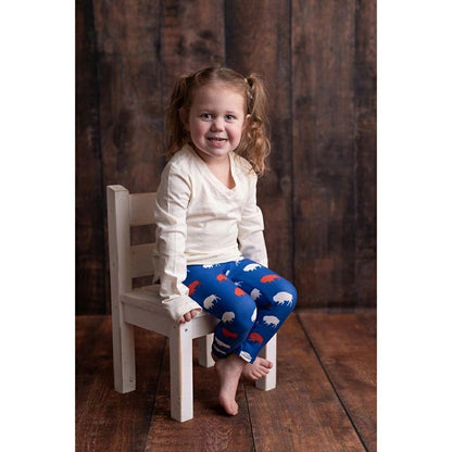 little girl sitting on white chair wearing royal blue, red, and white buffalo print leggings on wood background. 