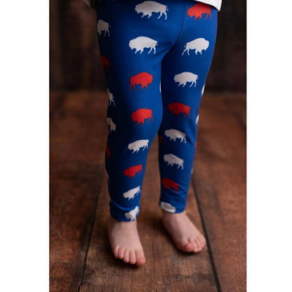 toddler standing wearing royal blue, red, and white buffalo print leggings on wood background. Little Gift Nook