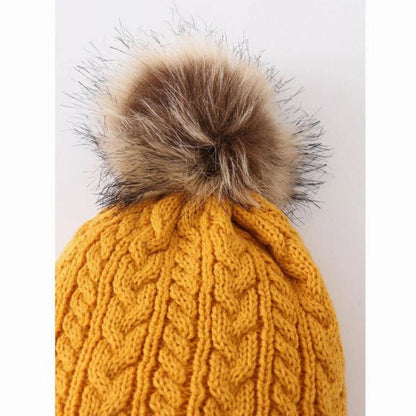 Close up of the Mustard cable knit pom pom on the child winter hat sitting on gray and white background.