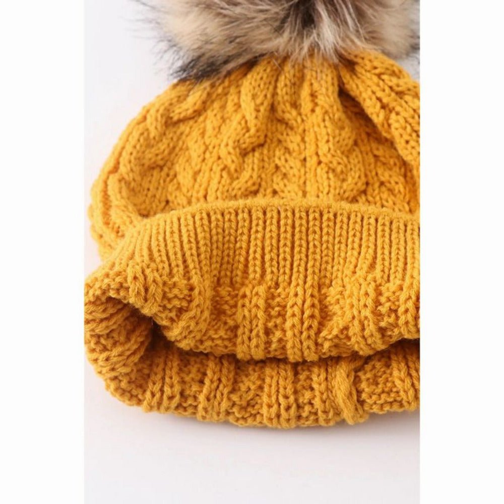 inside look of kids knit mustard beanie pom hat on white and gray background.