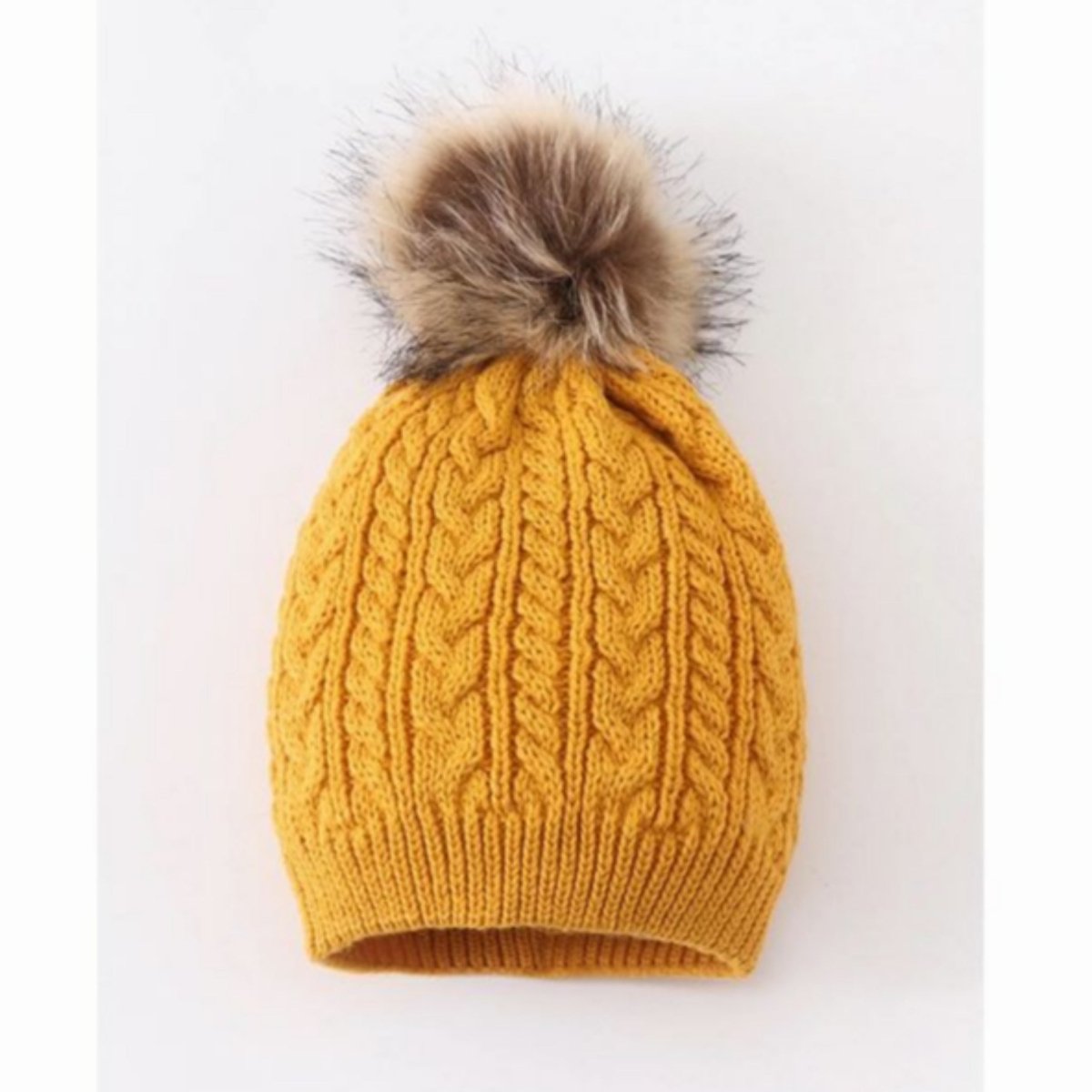 Mustard cable knit pom pom child beanie hat with tan faux fur pom at top on gray and white background.  - Little Gift Nook