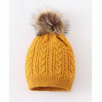 Mustard cable knit pom pom child beanie hat with tan faux fur pom at top on gray and white background.  - Little Gift Nook