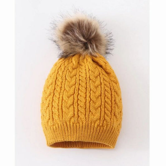 Mustard cable knit pom pom child beanie hat with tan faux fur pom at top on gray and white background.  - Little Gift Nook