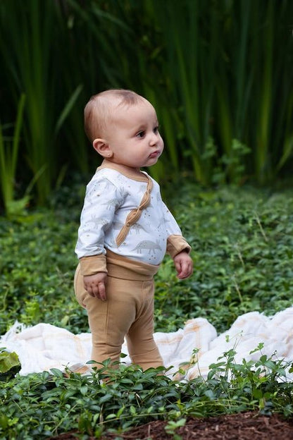 Baby standing up wearing tan infant leggins in a garden.