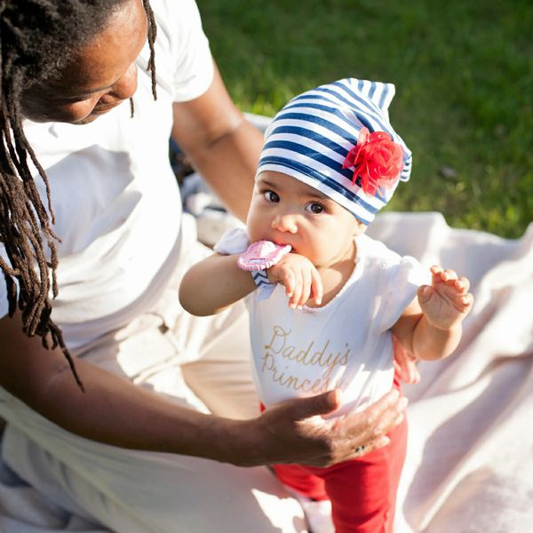 Baby held by mom with a Wristie Teether in pink on her wrist outdoors. 